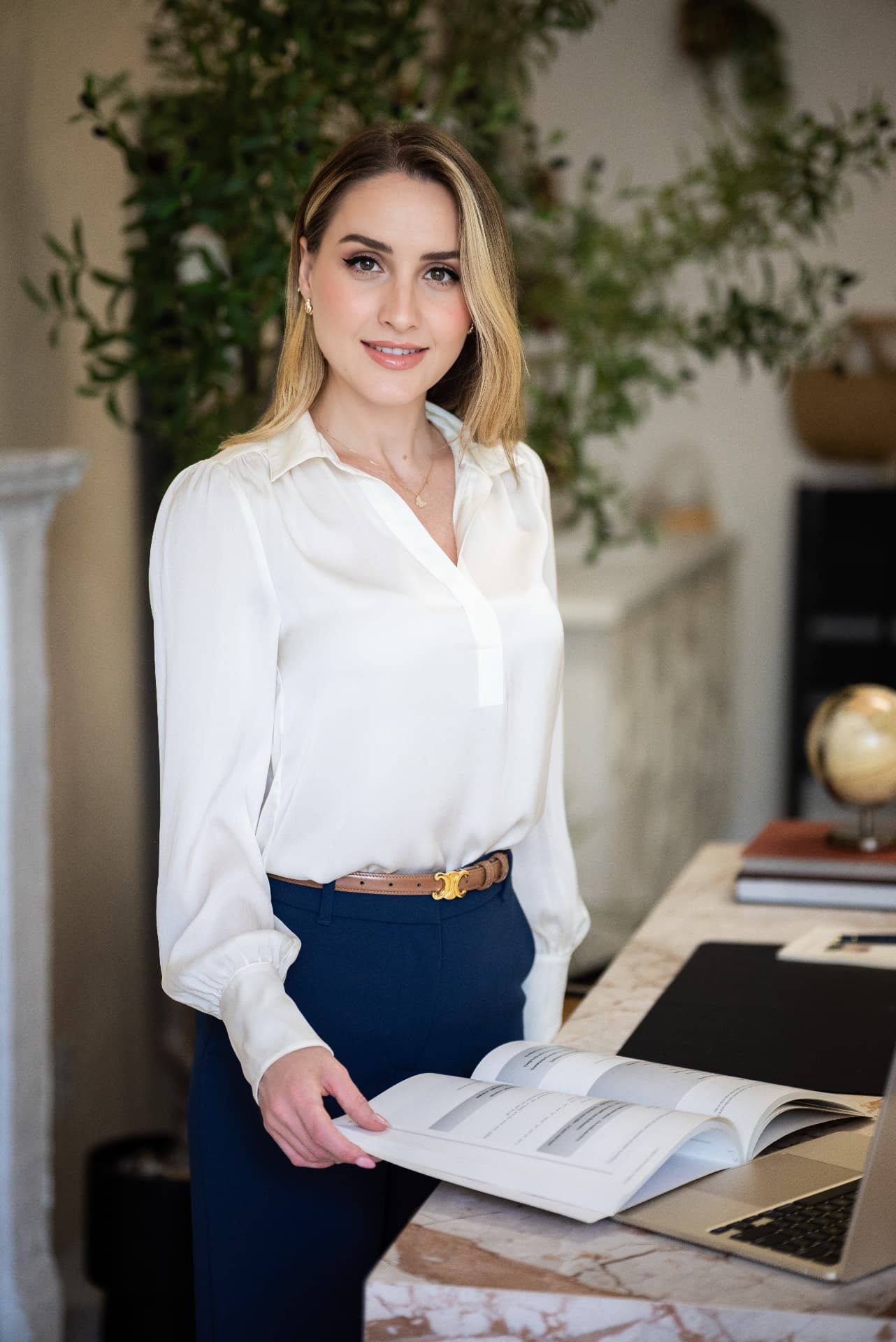 Iva Kadiu, founder and French coach at Lingo by Iva, standing beside an open French book and laptop.